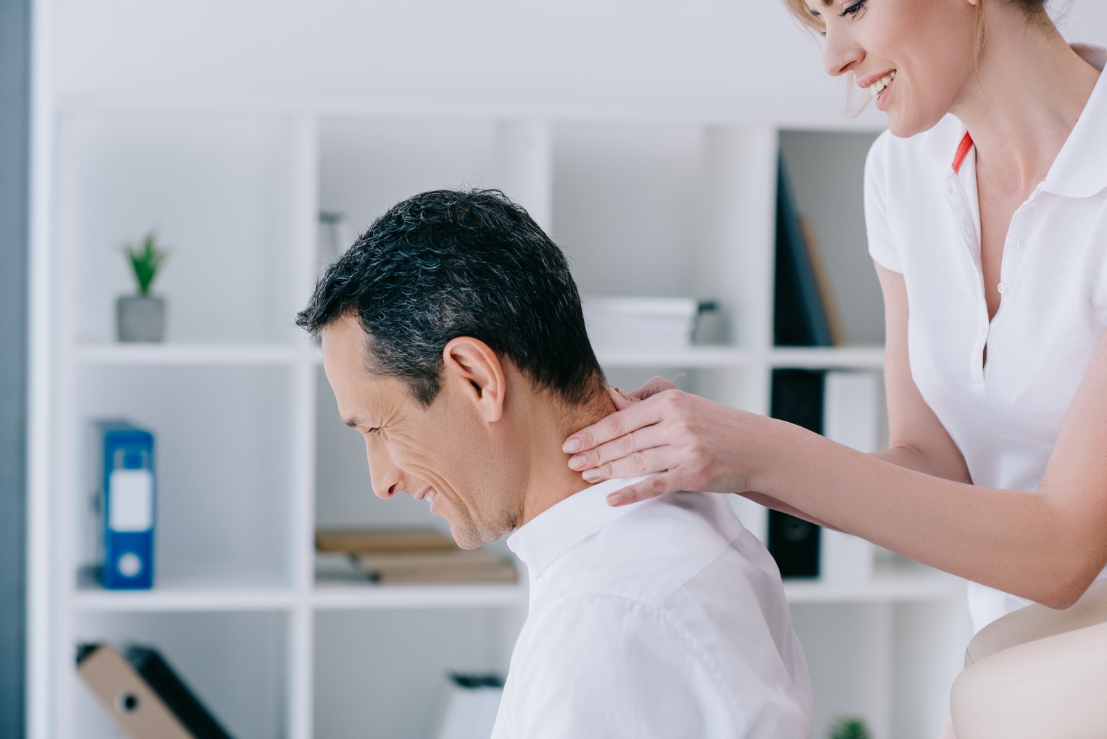 side view of masseuse doing seated neck massage for client at office Workplace massage At Desk Massage