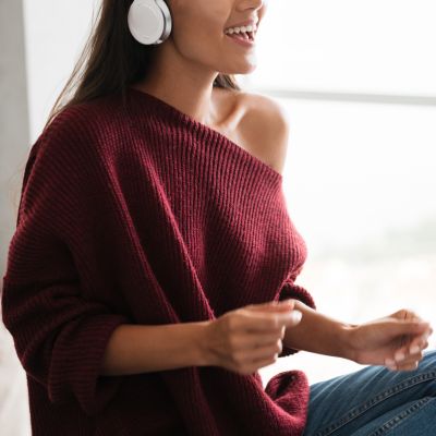 Happy pretty asian woman in headphones listening to music and singing while sitting on a kitchen table