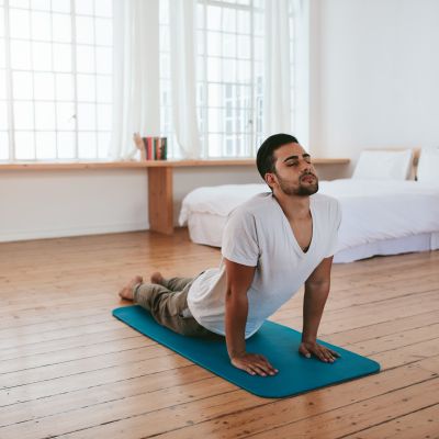 Indoor shot of handsome young man practicing yoga. Fitness man meditating with his eyes closed while doing cobra pose in living room.